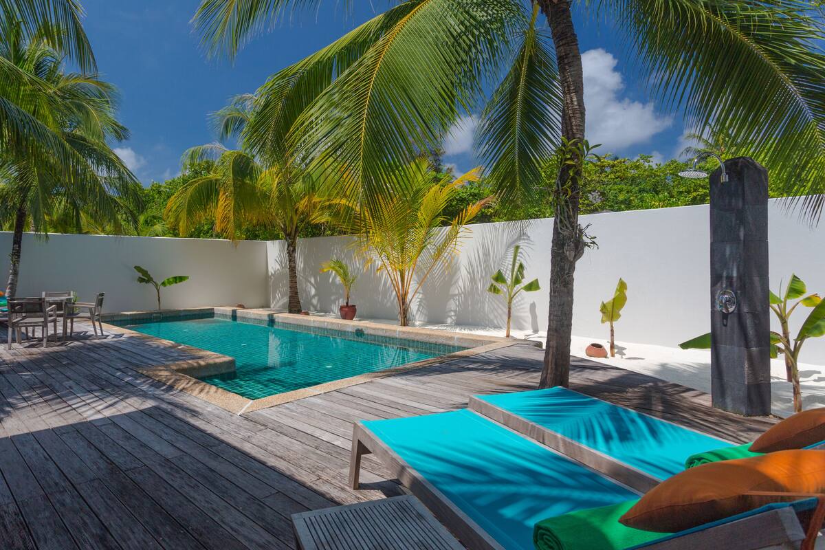 A wooden deck with a swimming pool, lounge chairs, and palm trees.