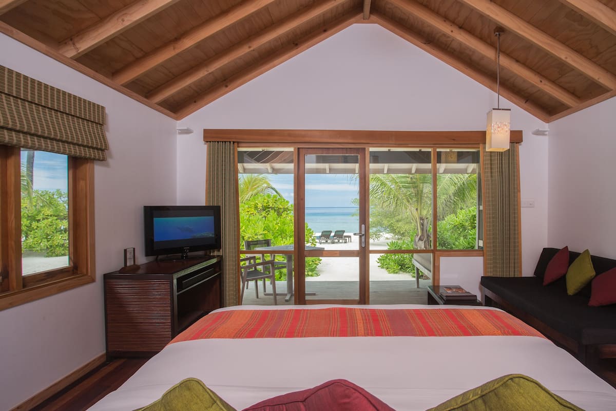 A bedroom with a large bed, a TV, and a view of the beach.