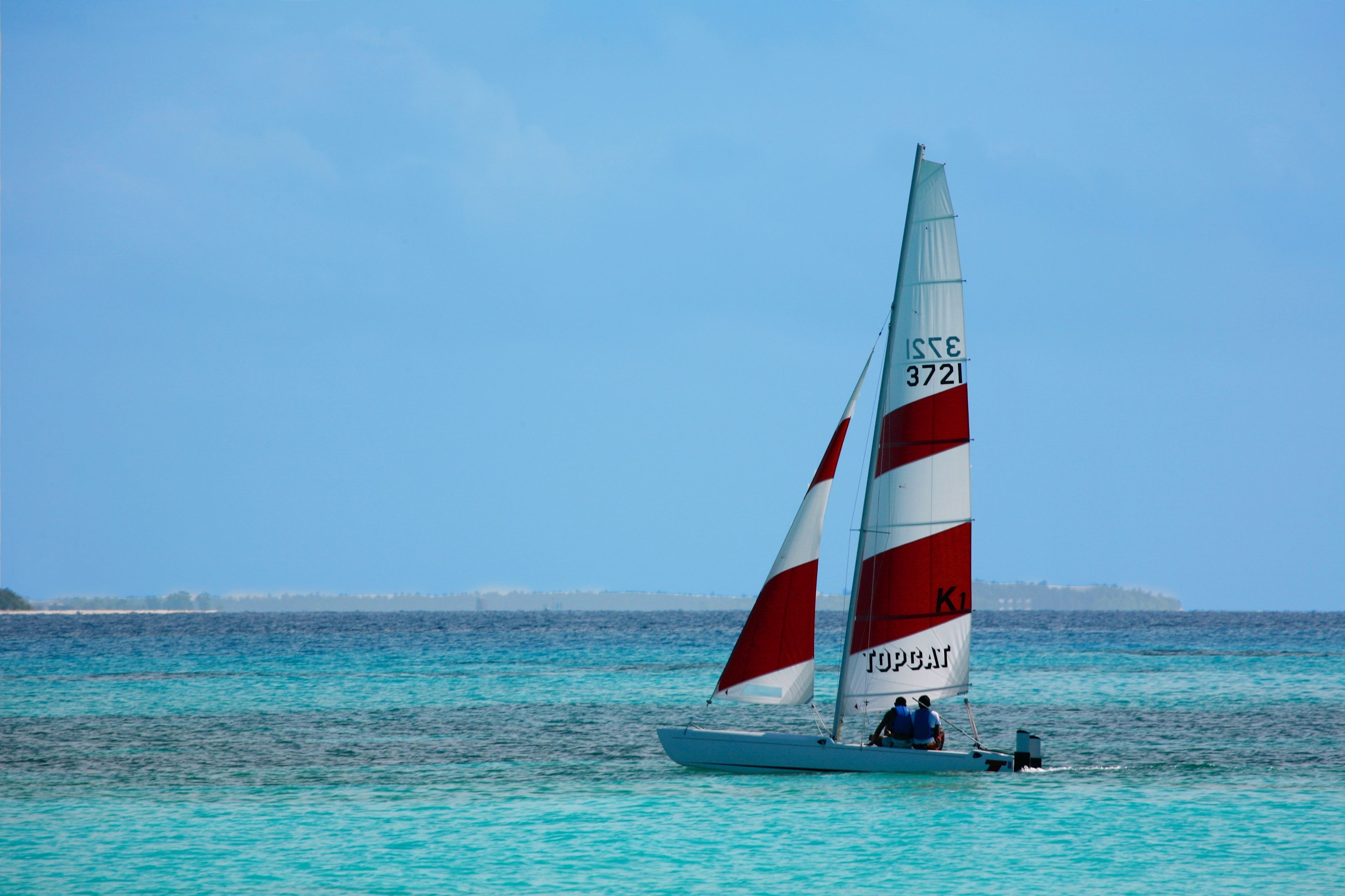 Ein Segelboot mit weißer und roter Segel, an der Seite mit "ISSE 3721" und "TOPEAN" beschriftet, fährt auf türkisfarbenem Wasser.