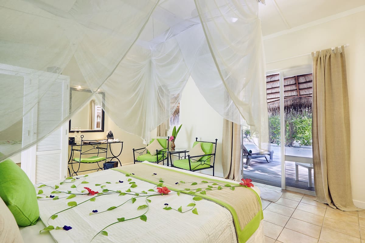 A bedroom with a bed, green chairs, a small table, and a view of the outdoors.