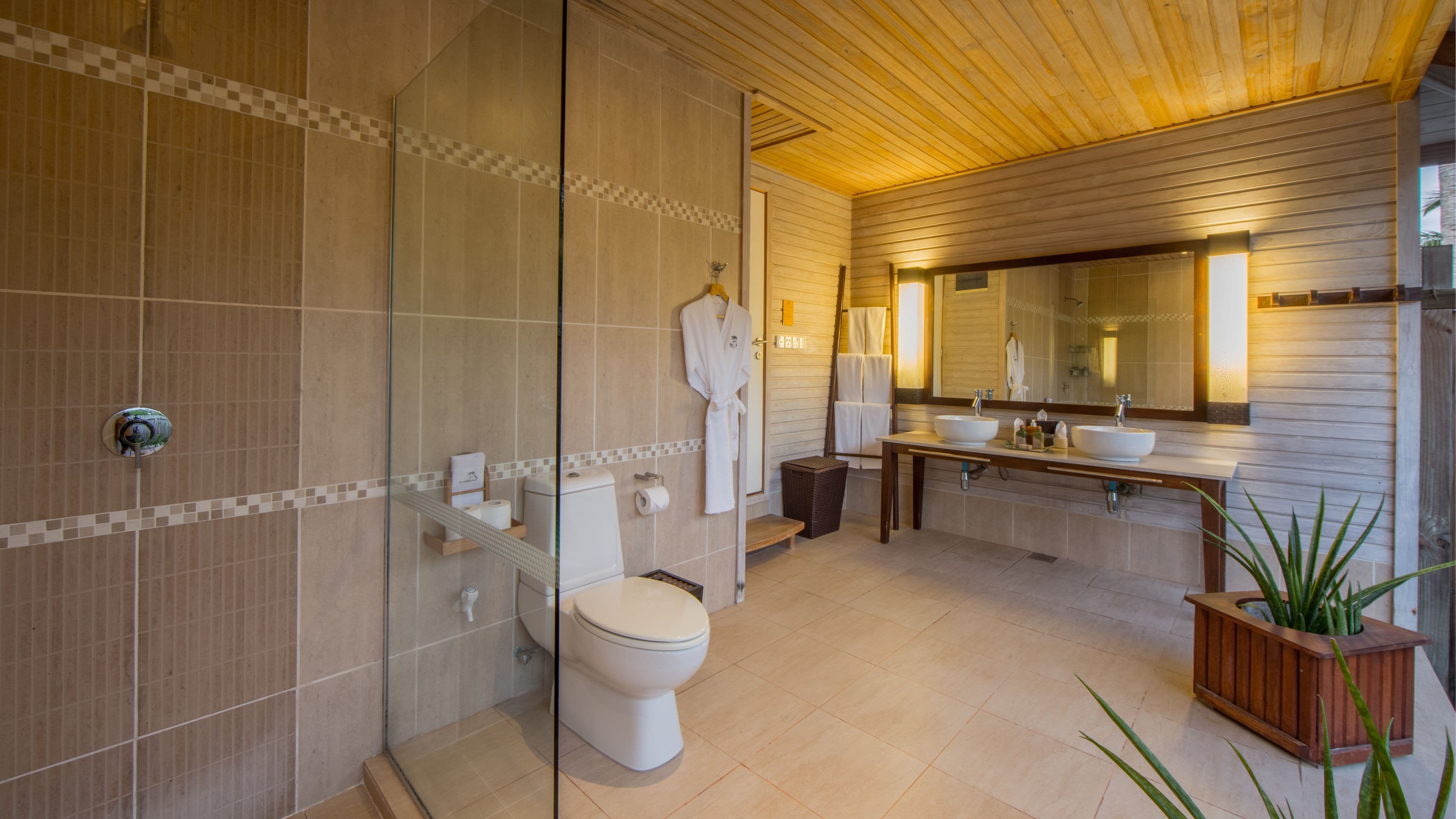 A modern bathroom with a glass shower enclosure, a toilet, a bidet, and a double sink vanity with a large mirror.