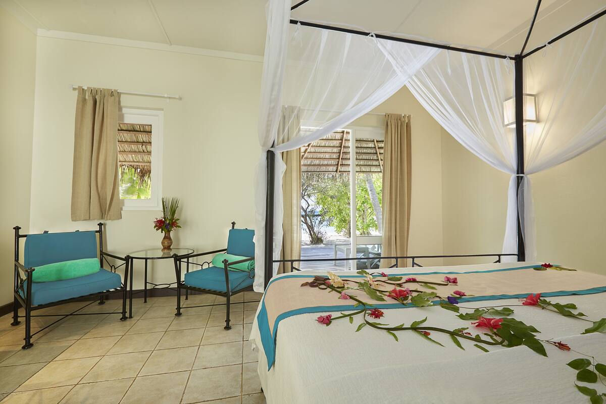 A room with a bed, a chair, a small table, and a window with curtains.