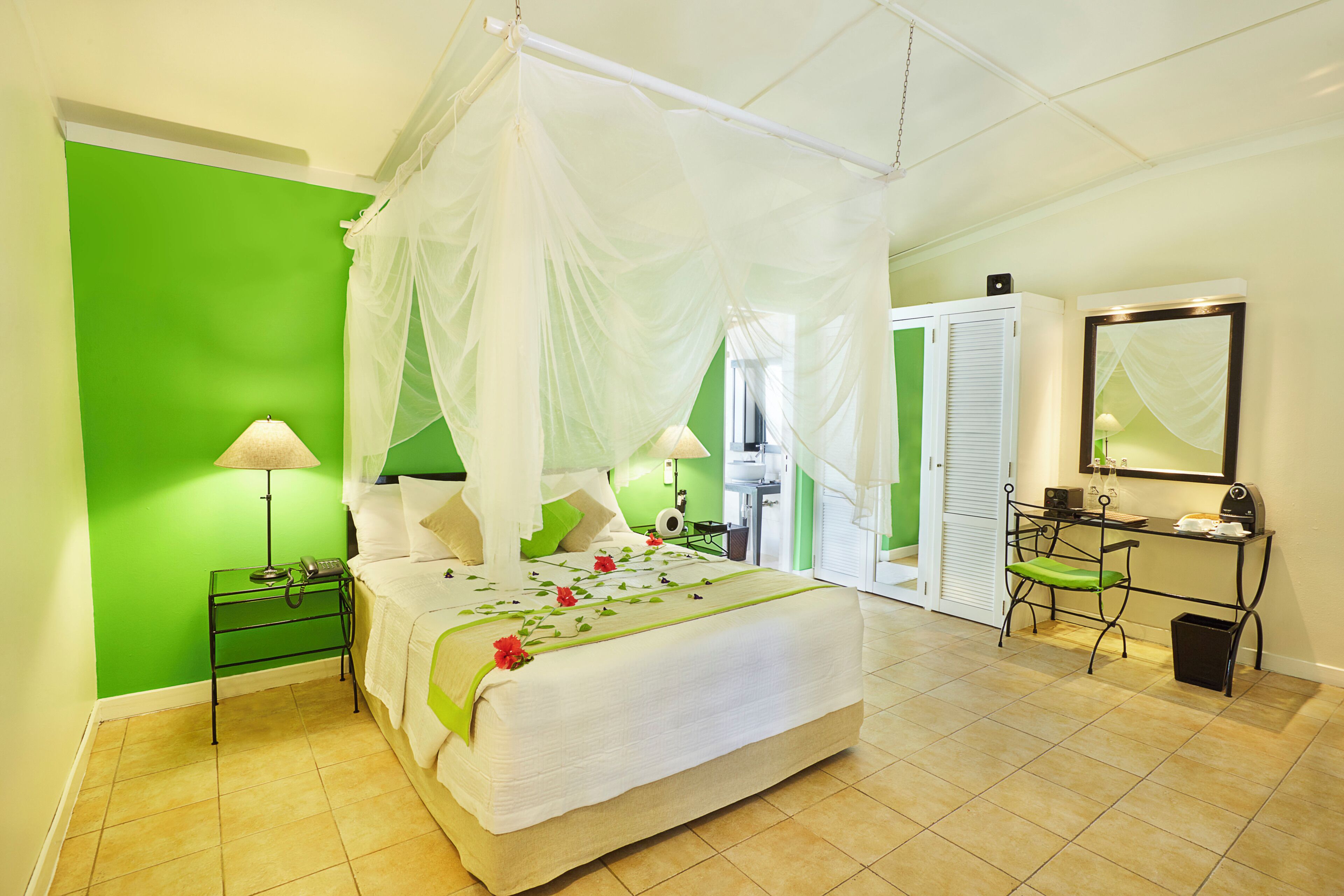 A room with a bed, green walls, a desk, and a mirror.