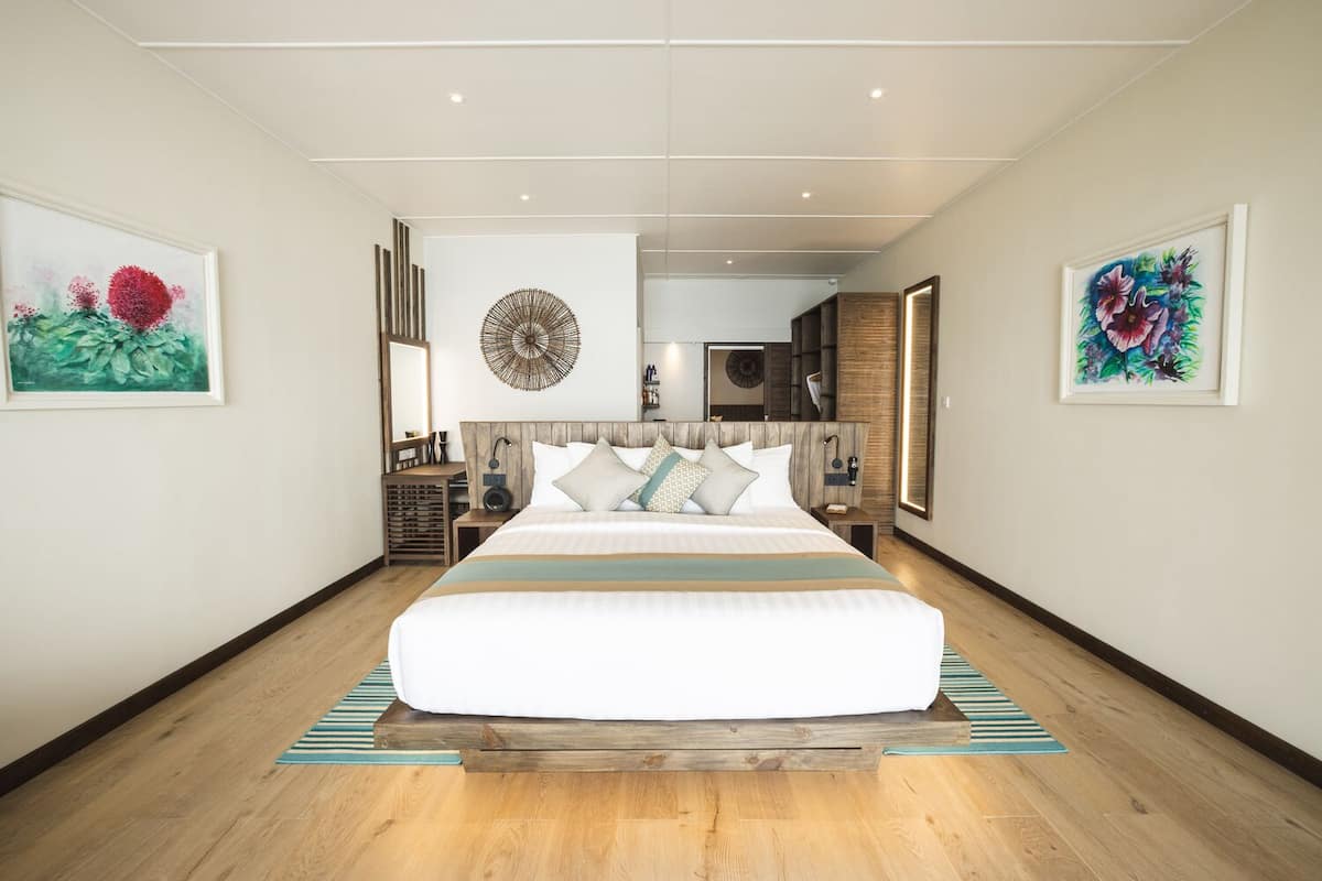 A modern hotel room with a large bed, wooden headboard, and a view into the hallway.