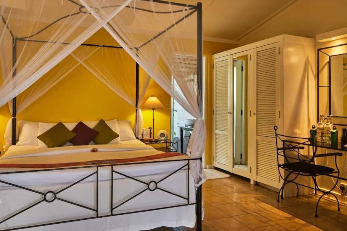 A bed with a canopy, a bedside table with a lamp, a chair, and a wardrobe.