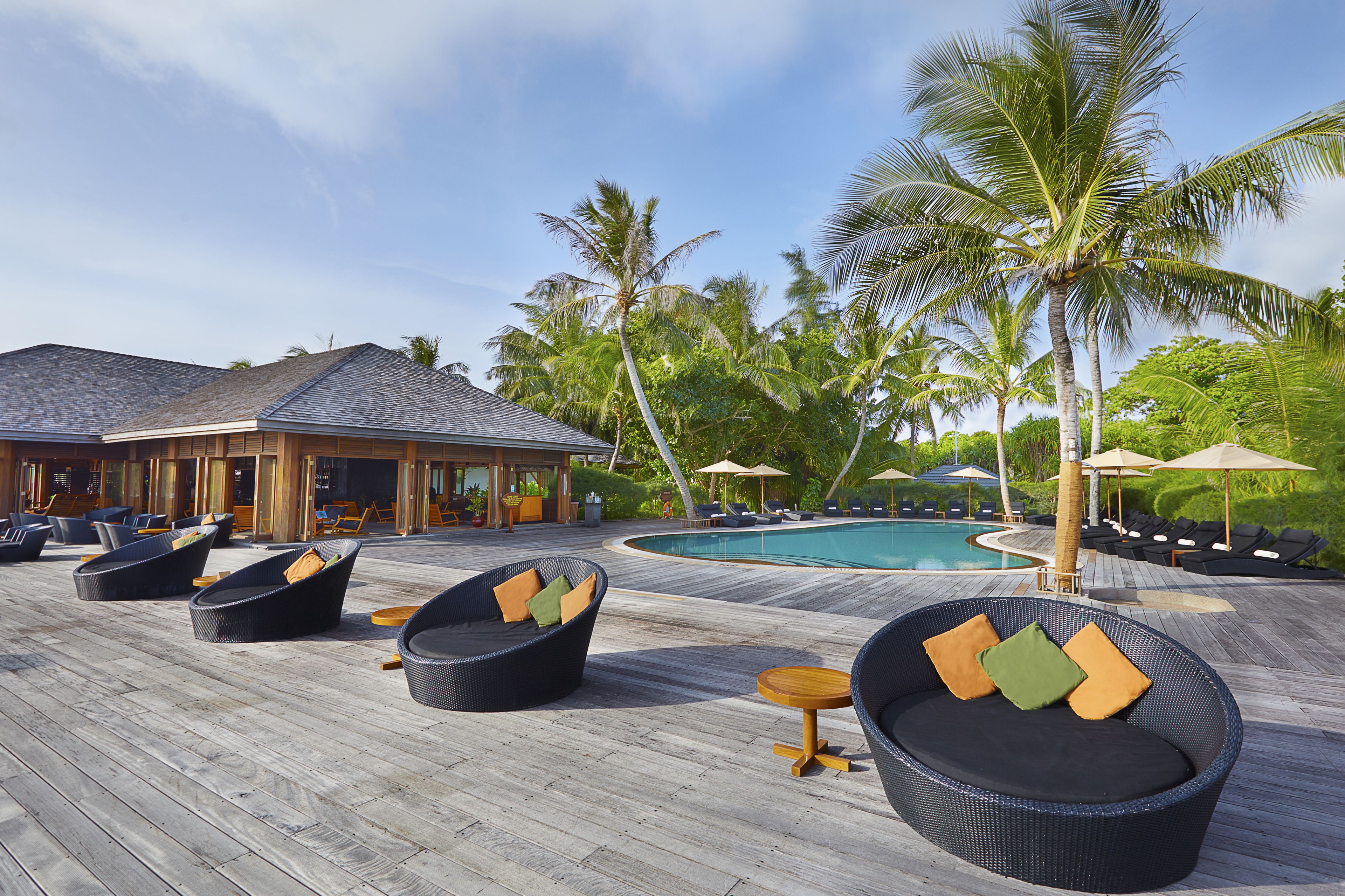 Un espace aménagé au bord de la piscine, avec des fauteuils de relaxation en osier et une terrasse en bois.