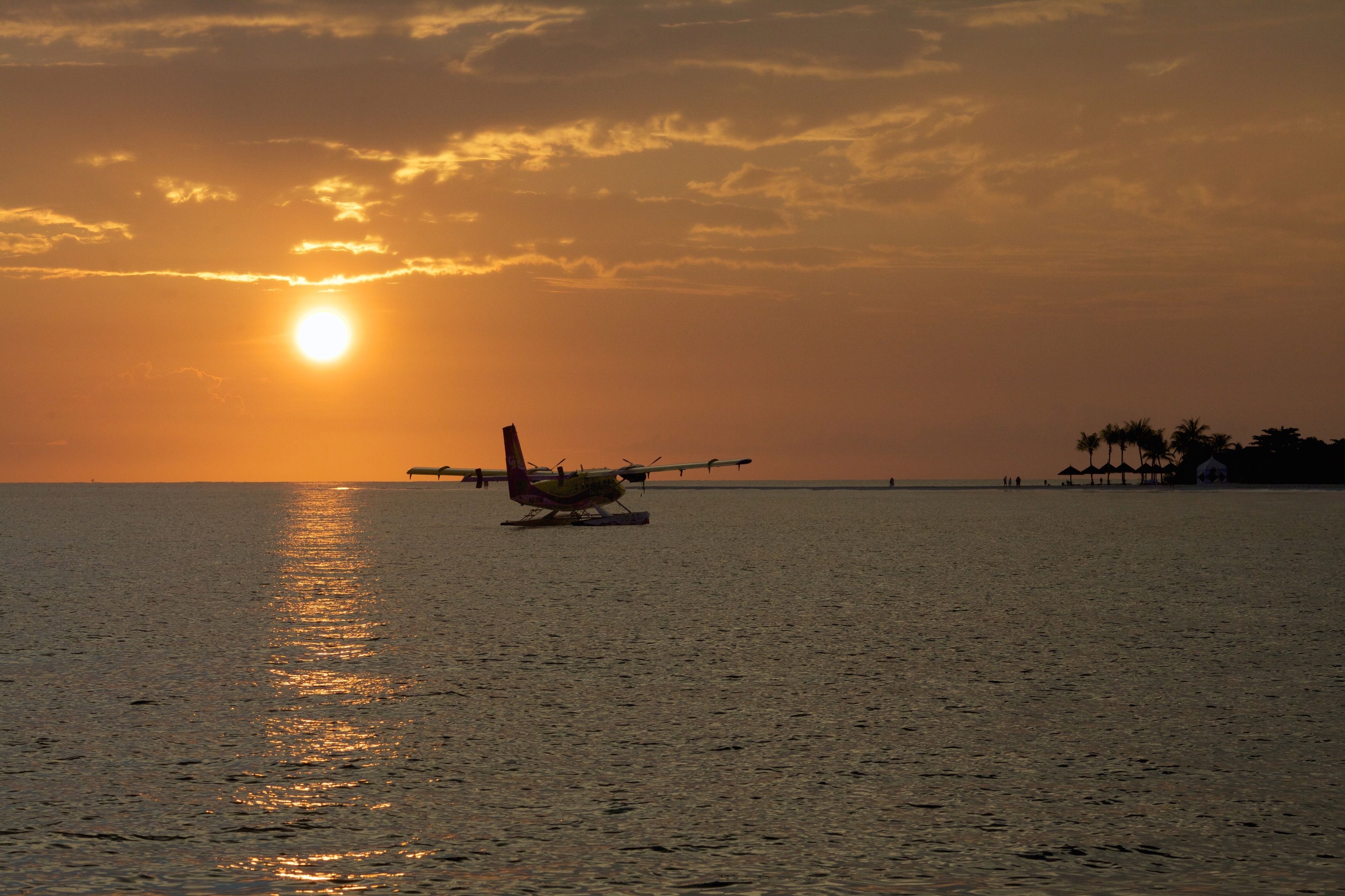 Un hidroavión sobre el agua con un atardecer al fondo.