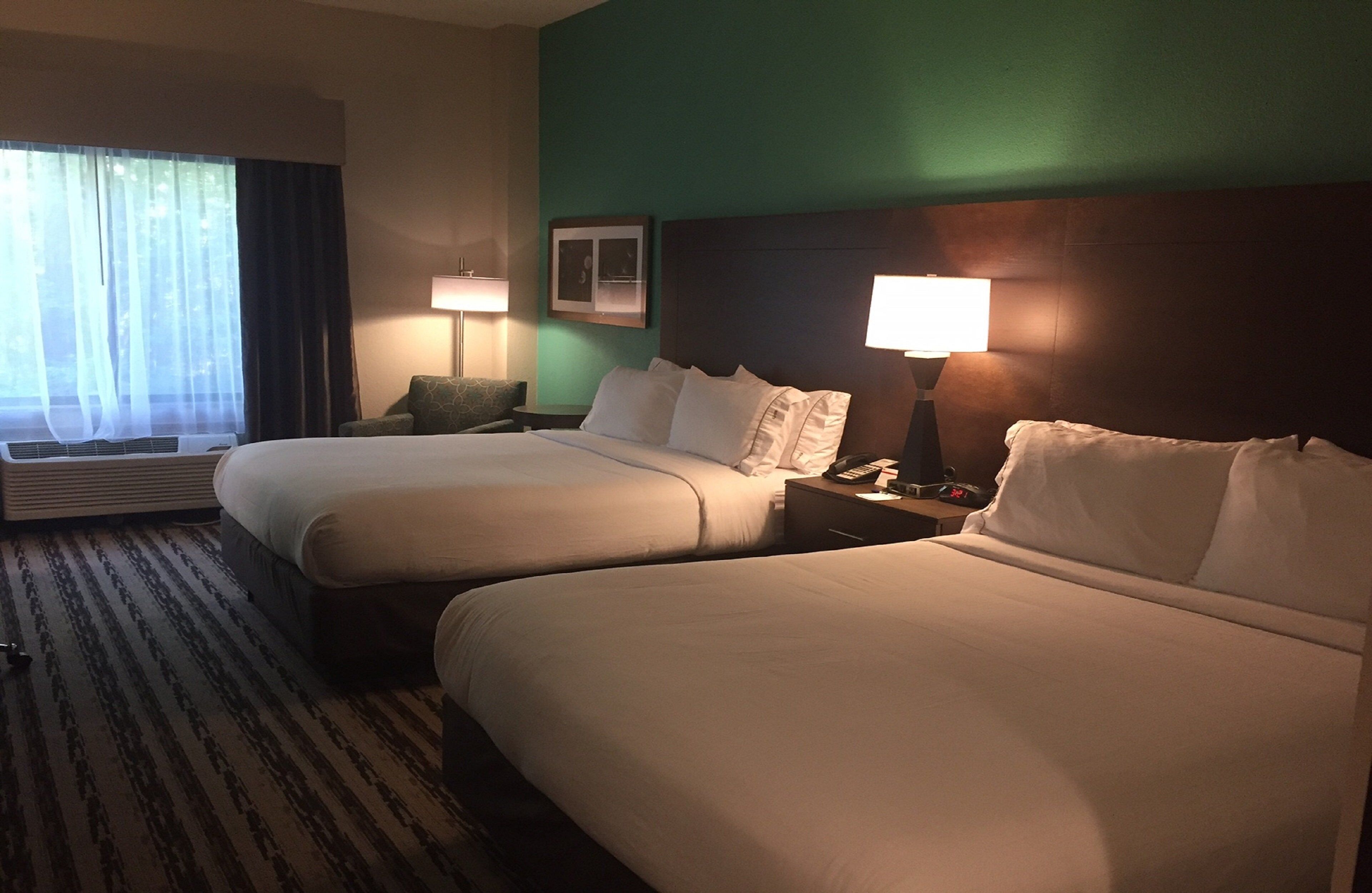 A hotel room with two beds, a desk, a chair, and a window with curtains.