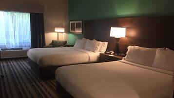 A hotel room with two beds, a desk, a chair, and a window with curtains.