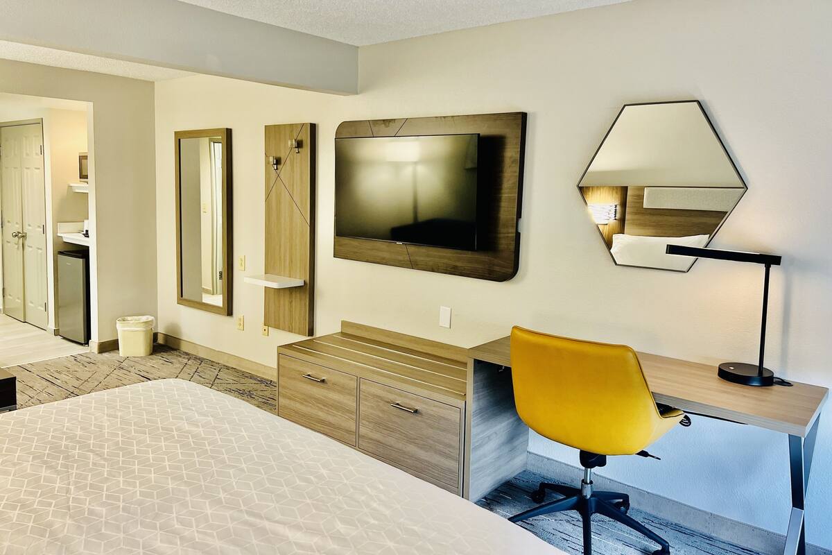 Ein Hotelzimmer mit Bett, Schreibtisch mit Stuhl, Fernseher, Spiegel und einem kleinen Schrank.