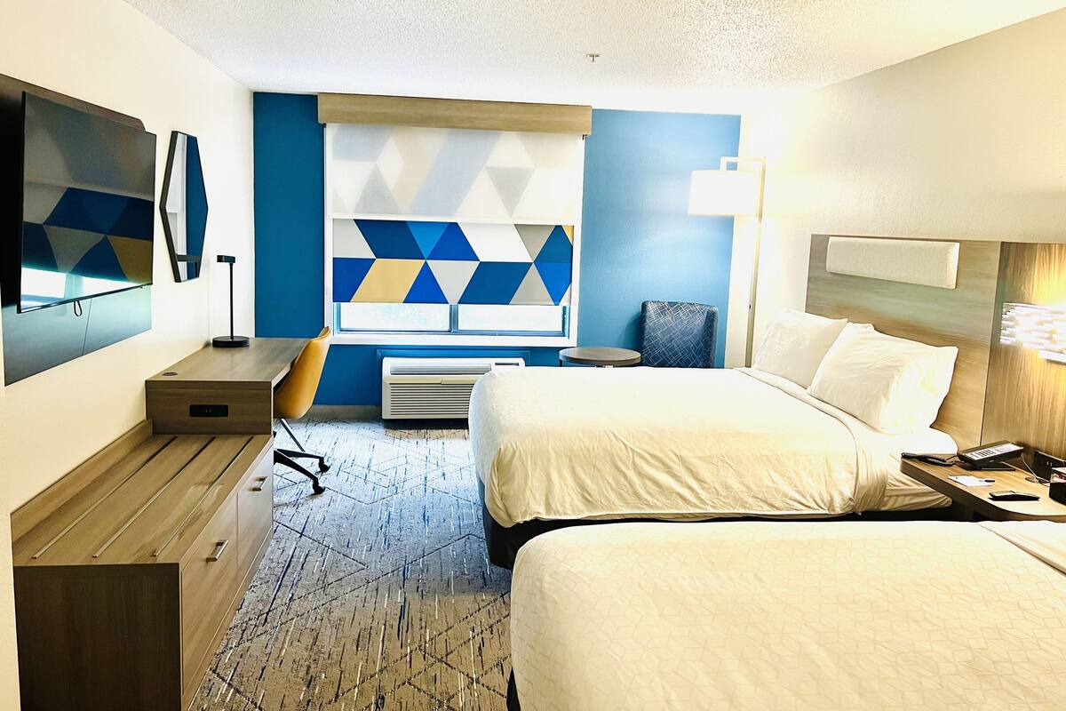 Ein Hotelzimmer mit Bett, Nachttisch, Lampe und einem an der Wand befestigten Fernseher.