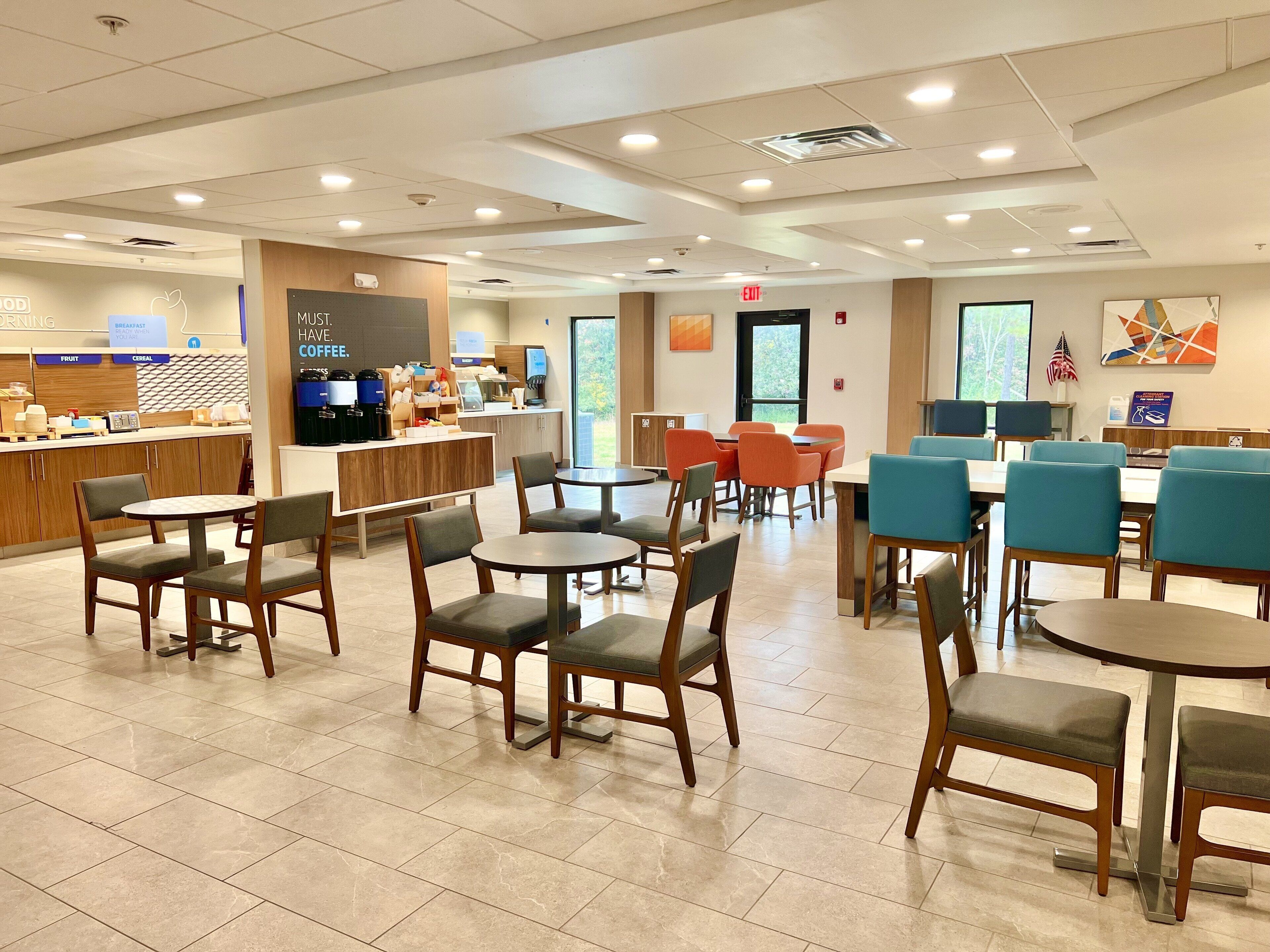 A spacious cafe with multiple seating areas, a counter with breakfast options, and a view of the outdoors.
