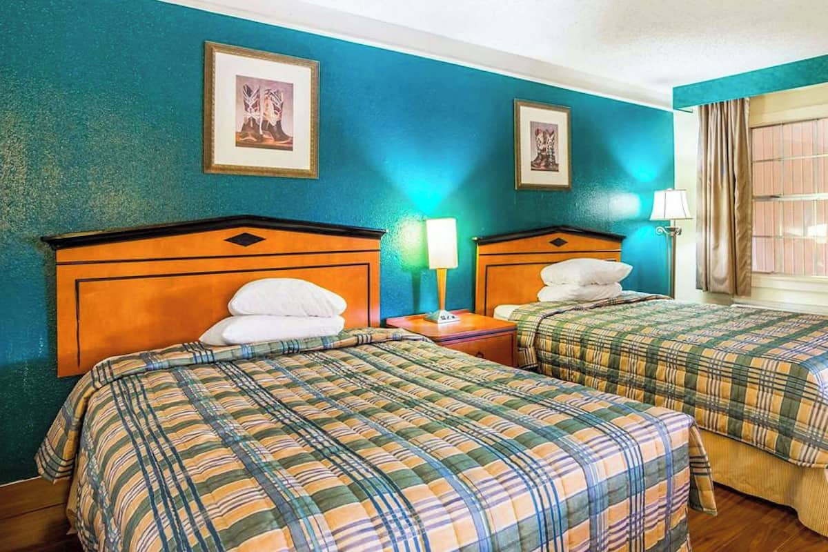 A hotel room with two beds, a nightstand with a lamp, and a window with curtains.