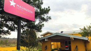 A MAGNUSON HOTEL sign with a star logo, located in a rural area with a yellow building in the background.