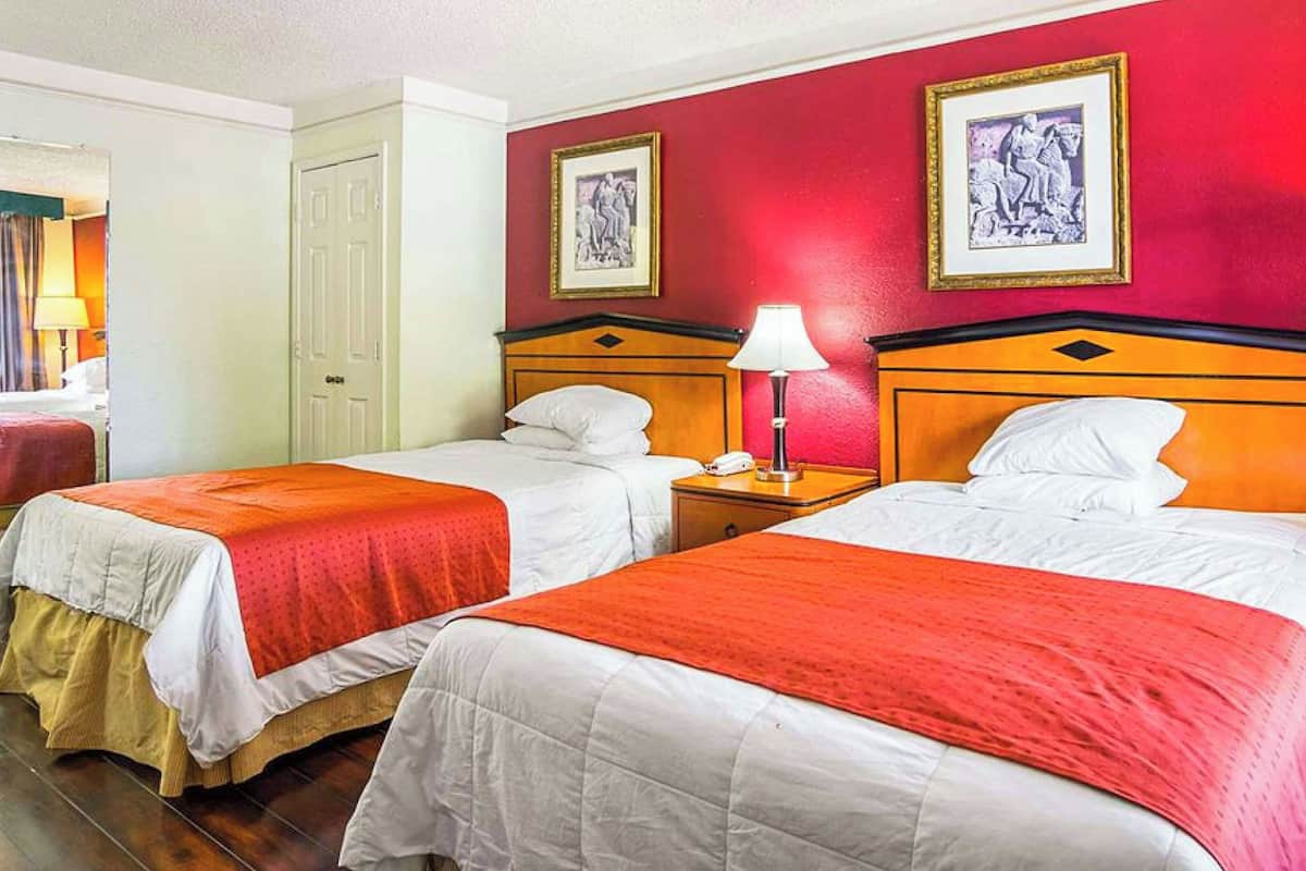 A hotel room with two beds, red walls, and framed artwork.