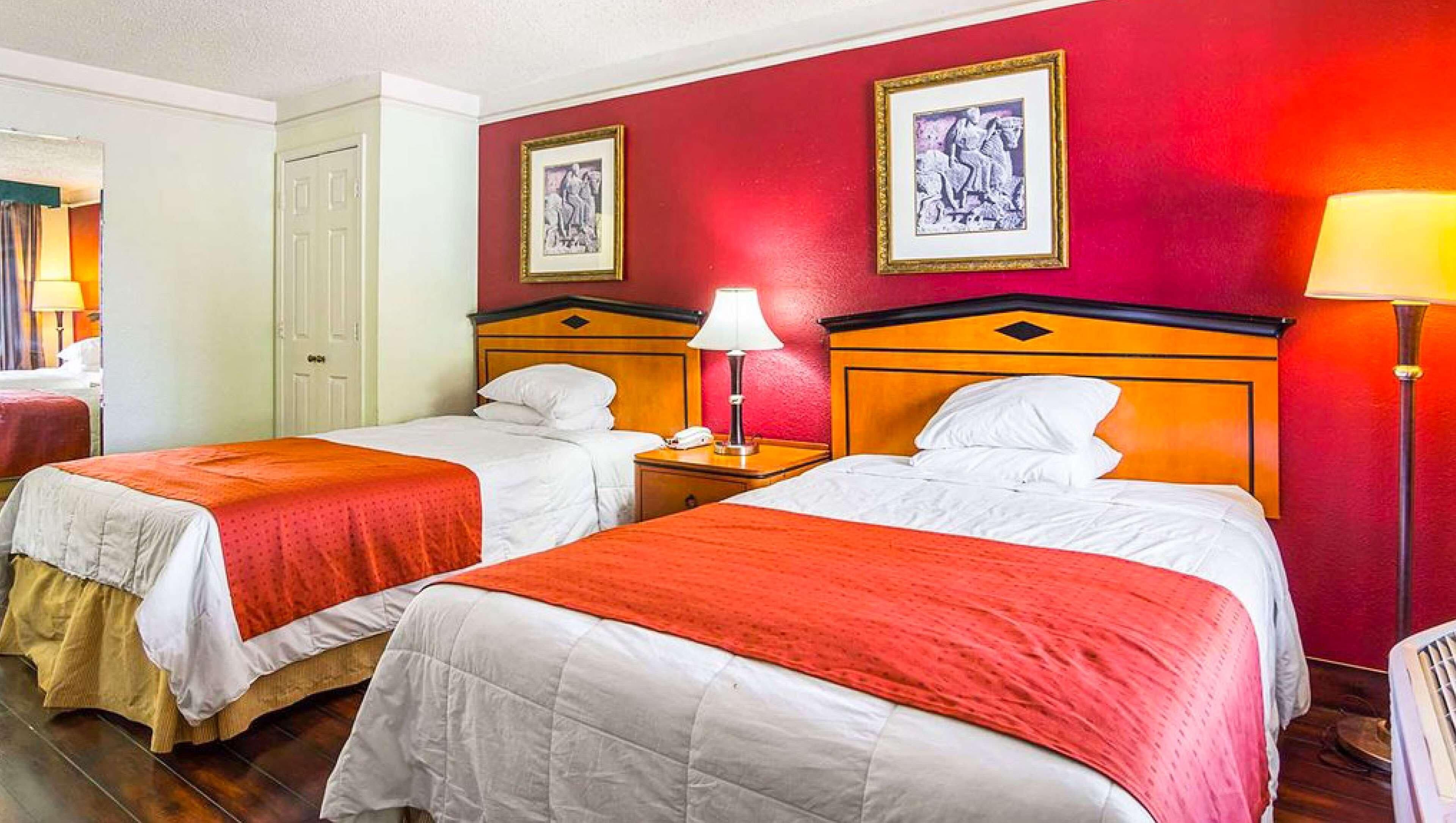 Een hotelkamer met twee bedden, rode wanden en kunstwerken in lijsten.