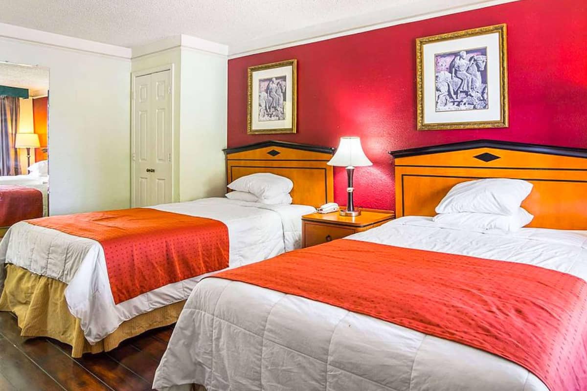 A hotel room with two beds, red walls, and framed artwork.