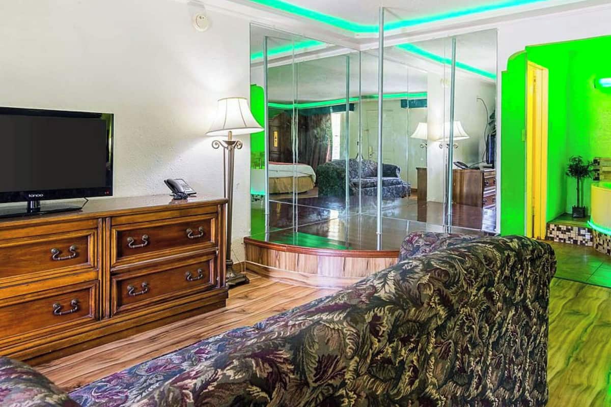 A modern living room with a flat-screen TV, wooden furniture, a patterned sofa, a glass partition, and a green accent wall.