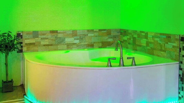 A large, oval-shaped hot tub with two faucets, set against a wall with a mosaic tile pattern.