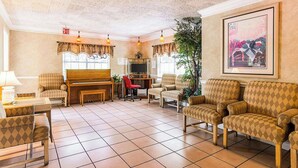 A living room with a piano, multiple armchairs, a television, and a framed picture on the wall.