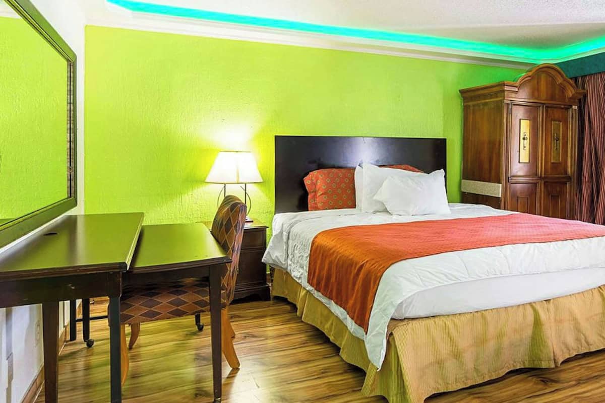 A hotel room with a bed, a desk, a chair, a wardrobe, and a lamp.
