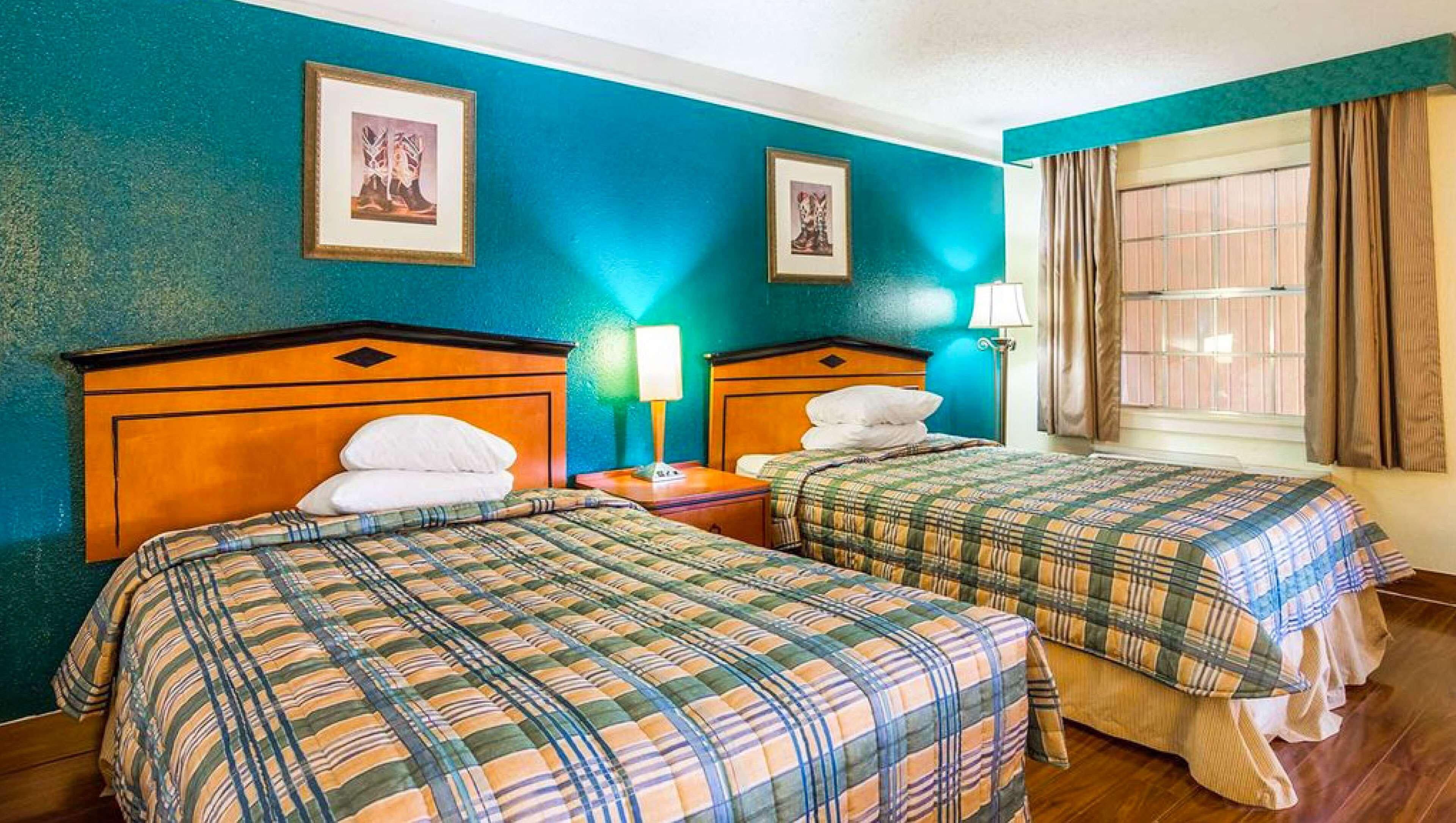 Een hotelkamer met twee bedden, teal muren, ingelijste foto's en een raam met gordijnen.