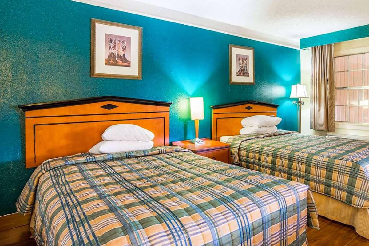 A hotel room with two beds, teal walls, framed pictures, and a window with curtains.