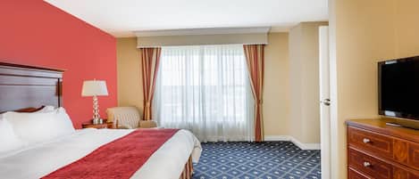 Habitación de hotel con una cama grande, televisión, cómoda y ventana con cortinas.