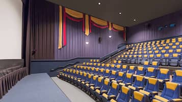 A theater with rows of blue and yellow seats, a stage, and a staircase leading to the upper seating.