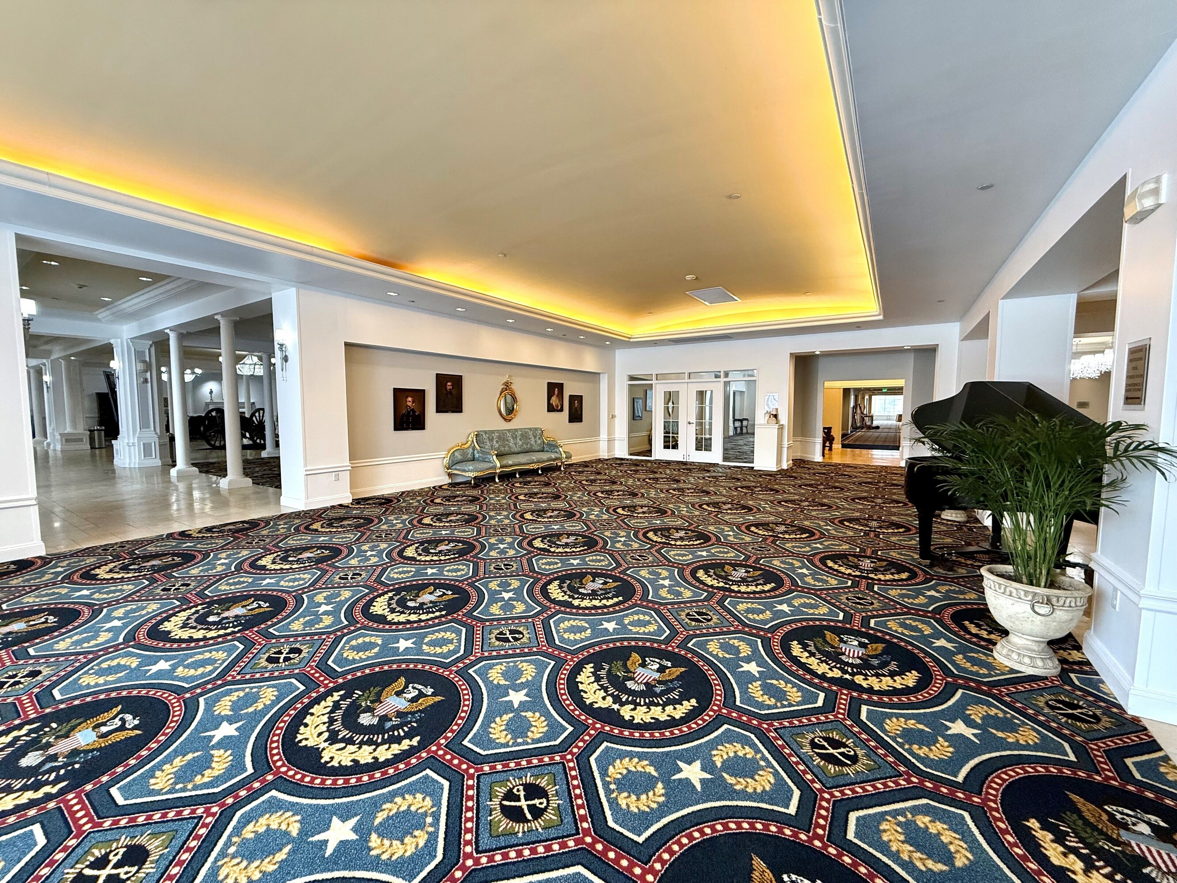 A spacious lobby with a patterned carpet, a grand piano, and a potted plant.
