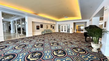 A spacious lobby with a patterned carpet, a grand piano, and a potted plant.