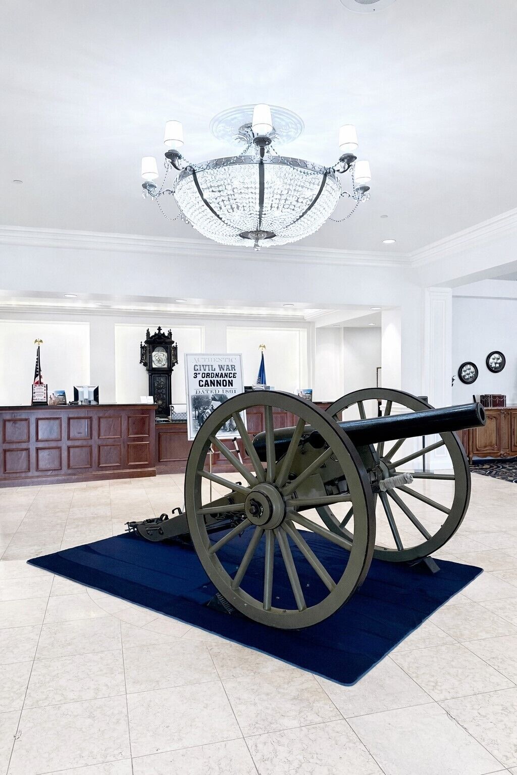 A cannon in a spacious lobby with a chandelier, a clock, and a sign about the Civil War cannon.