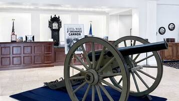 A cannon in a spacious lobby with a chandelier, a clock, and a sign about the Civil War cannon.