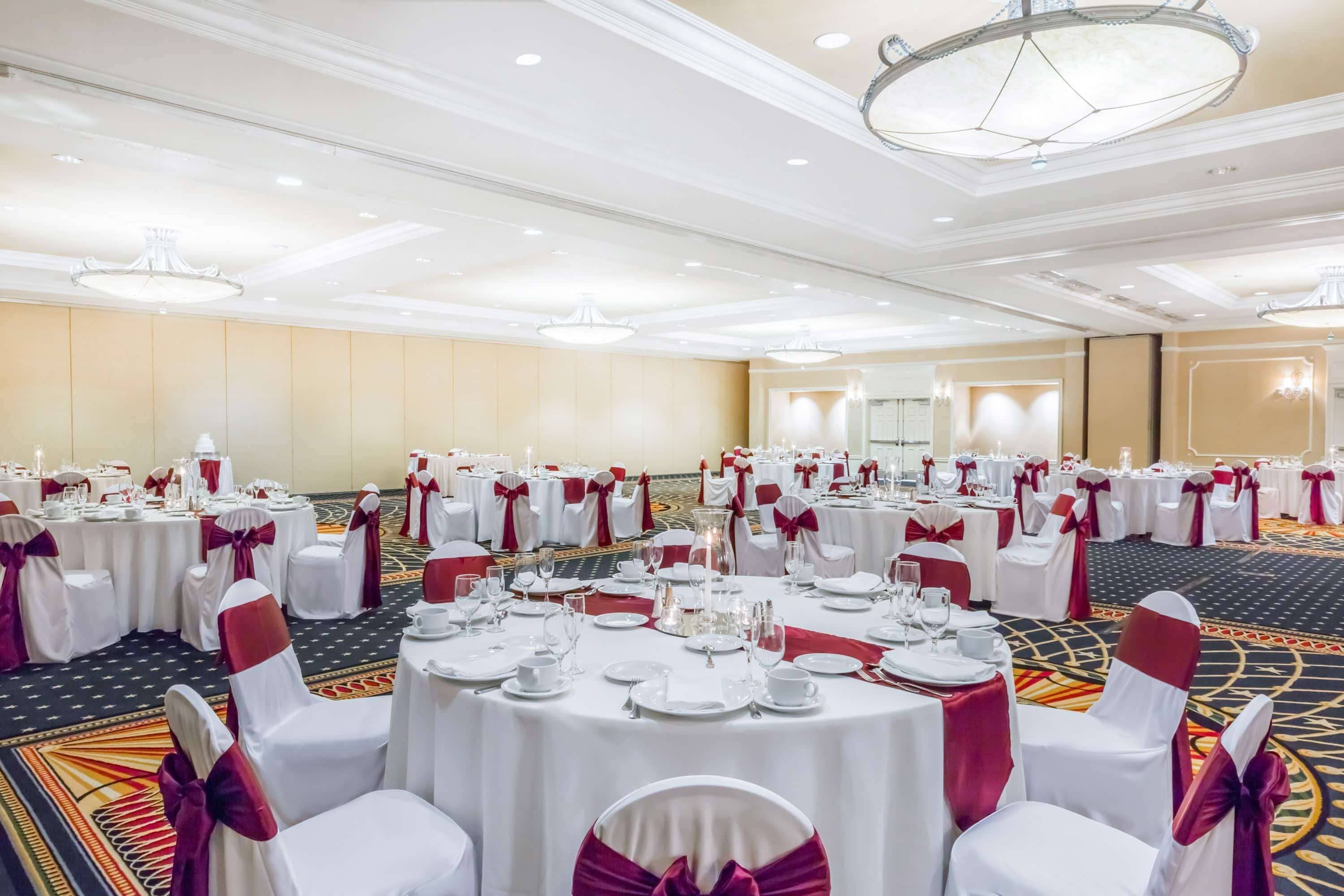 A banquet hall with round tables set for a formal event, featuring white tablecloths and red sashes.