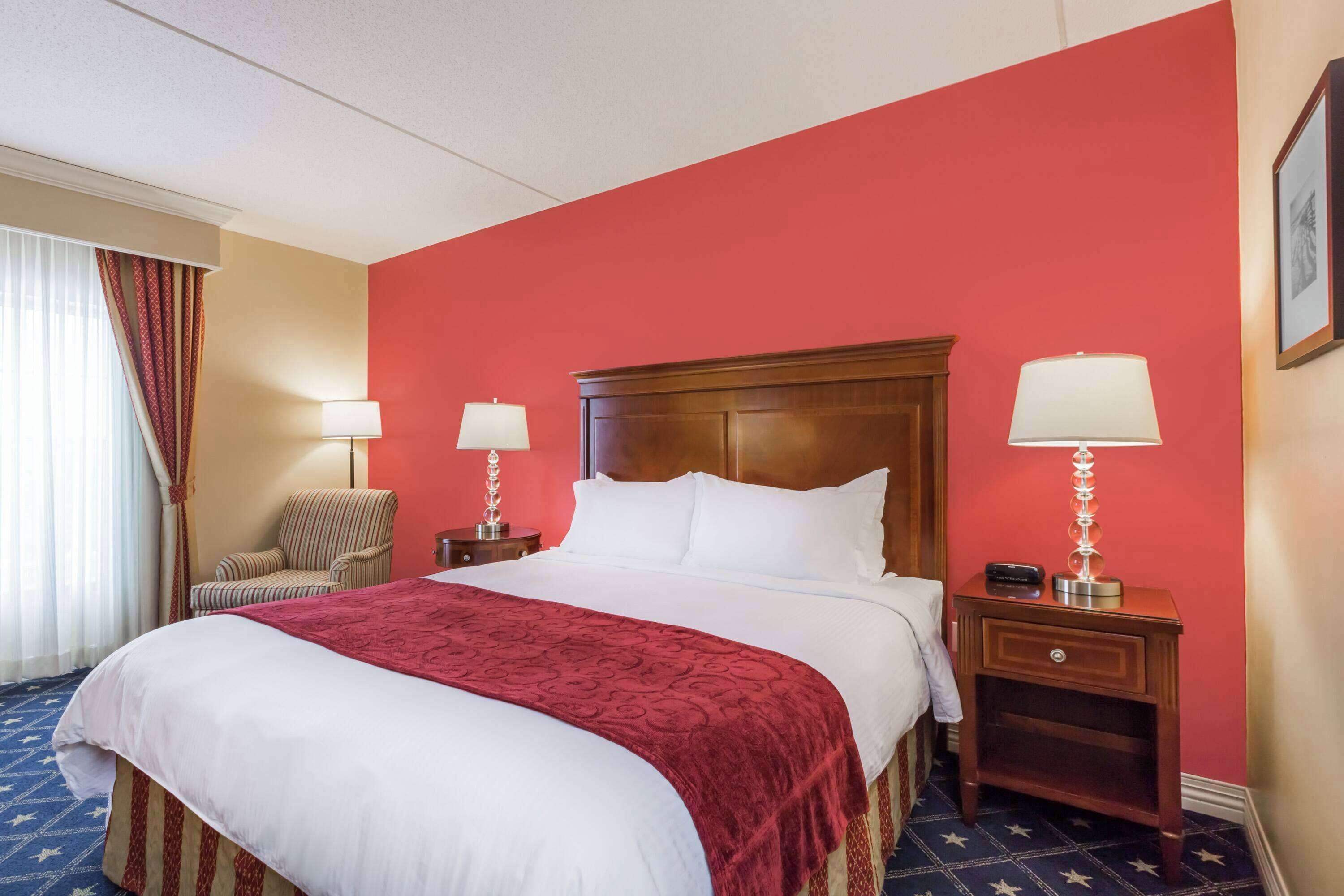 A hotel room with a large bed, two bedside tables with lamps, a chair, and a window with curtains.