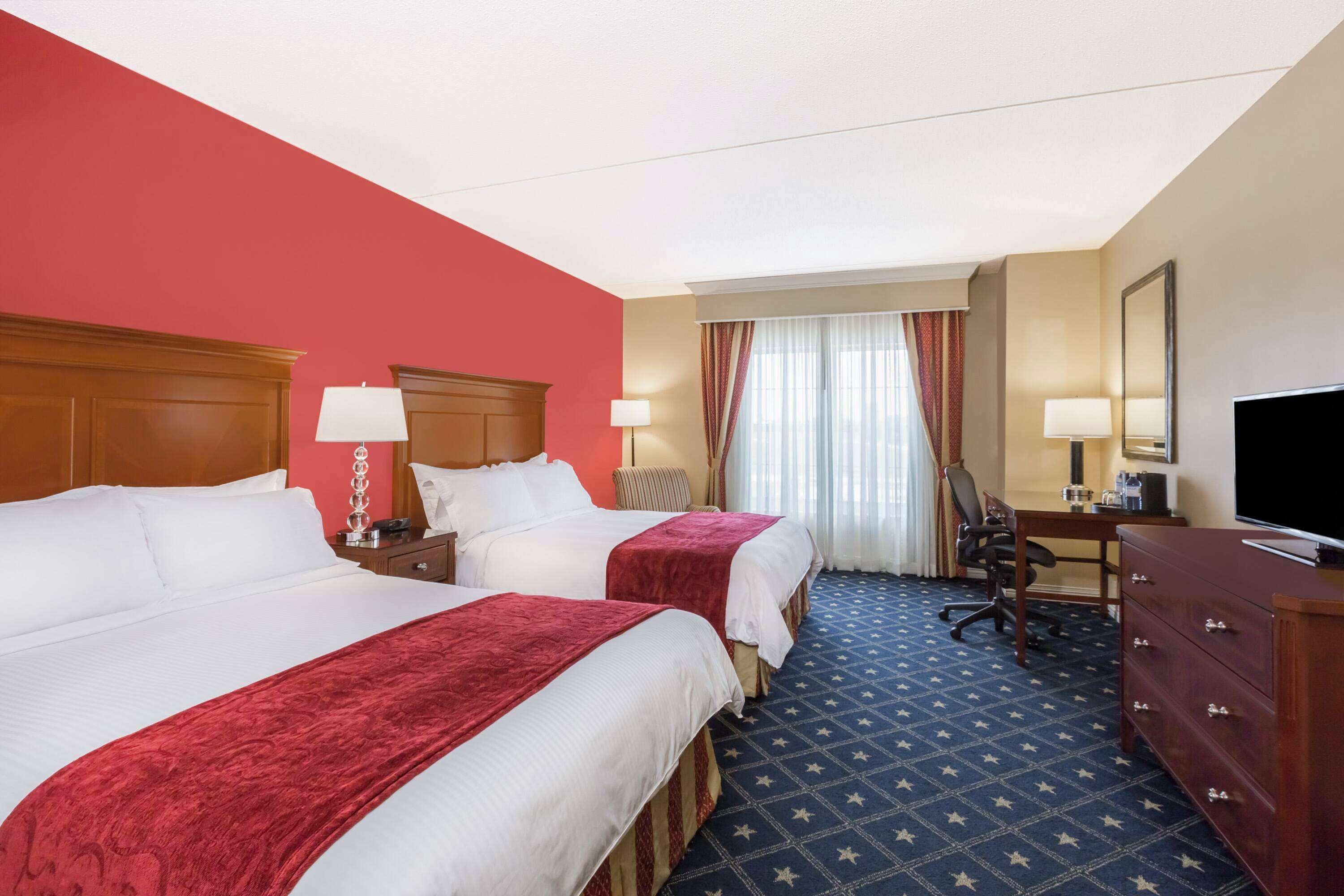 A hotel room with two beds, a desk with a chair, a television, and a dresser.