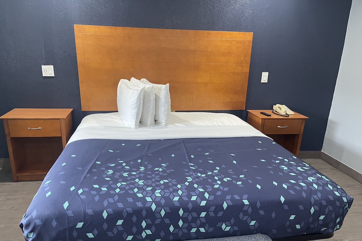 A neatly made bed with a patterned bedspread, wooden headboard, and two bedside tables with a phone on one.