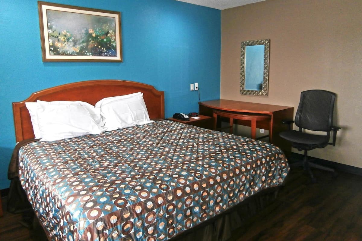A hotel room with a bed, a desk, a chair, a painting, and a mirror.