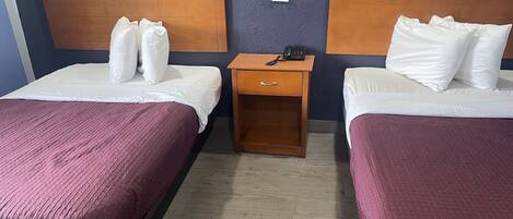 Habitación de hotel con dos camas, cada una con cabecero de madera, una mesita de noche de madera con un teléfono, e interruptor de luz en la pared.