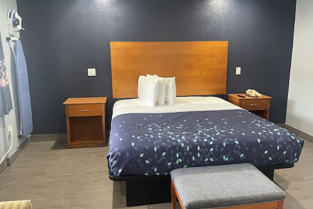 A hotel room with a bed, bedside tables, a bench, and a wall-mounted telephone.