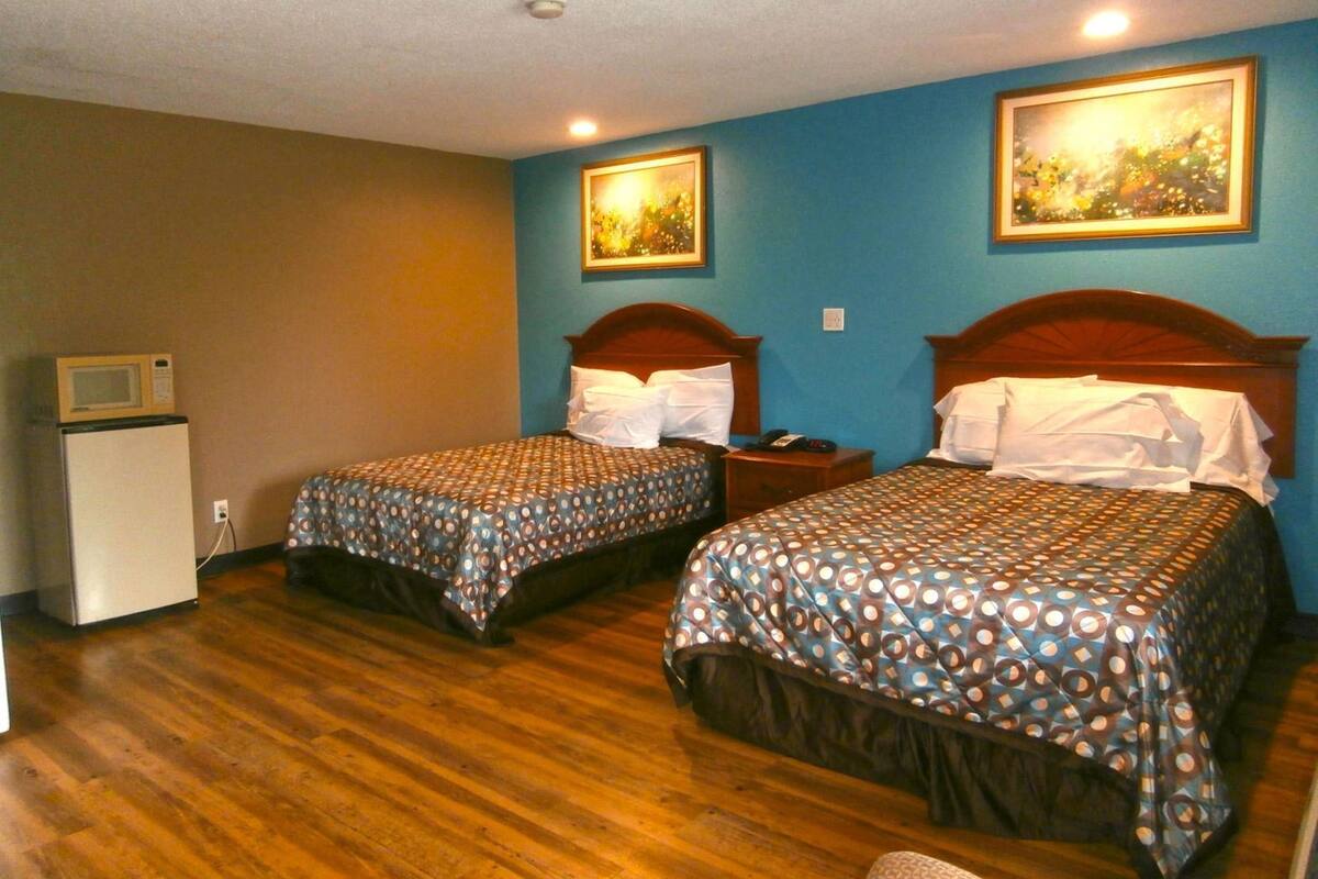 A hotel room with two beds, wooden headboards, a small white refrigerator, and two framed pictures on the wall.