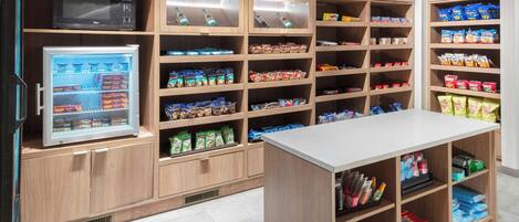 A well-organized snack and beverage area with shelves stocked with various products, a refrigerator, and a microwave.