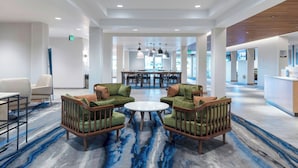 A spacious lobby with a central seating area featuring green upholstered chairs, a round table, and a blue marble-patterned floor.