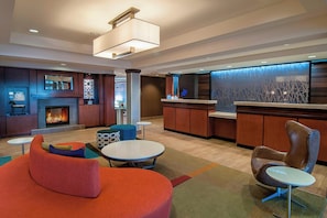 Eine moderne Lobby mit Kamin, Sitzbereichen, einer Rezeption und einer dekorativen Wand.