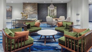 A modern lounge area with green upholstered chairs, a round coffee table, and a stone accent wall.