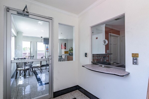 A hotel lobby with a glass door leading to a dining area, a small kitchen counter, and a 'RING BELL FOR SERVICE' sign.