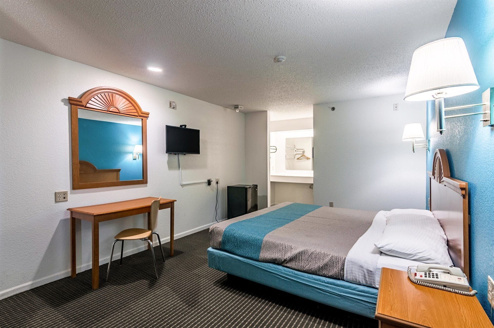 Une chambre d’hôtel équipée d’un lit, d’un bureau, d’une chaise, d’une télévision, d’un miroir, d’une lampe et d’un téléphone.