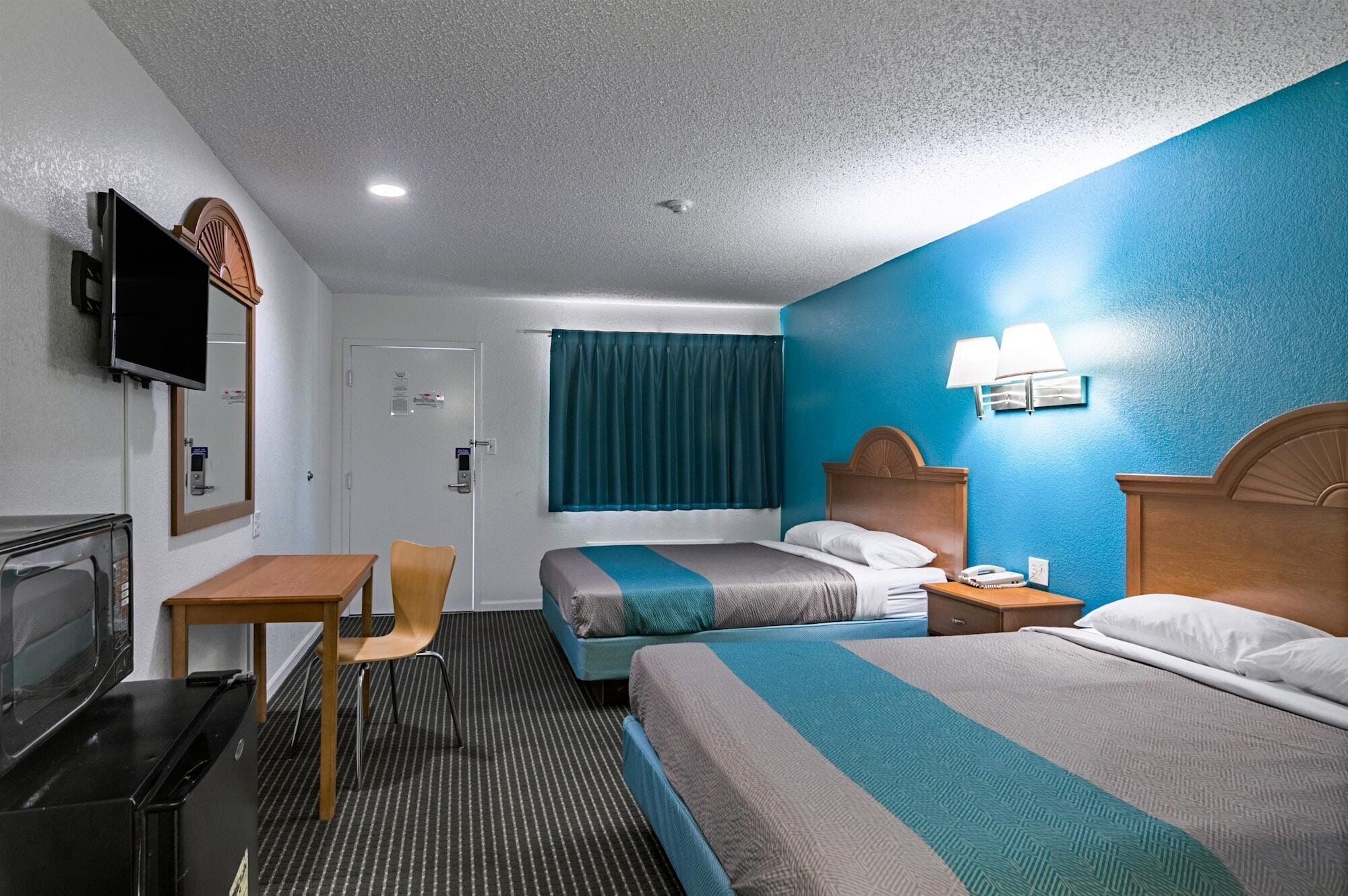A hotel room with two beds, a desk, a chair, a TV, and a microwave.