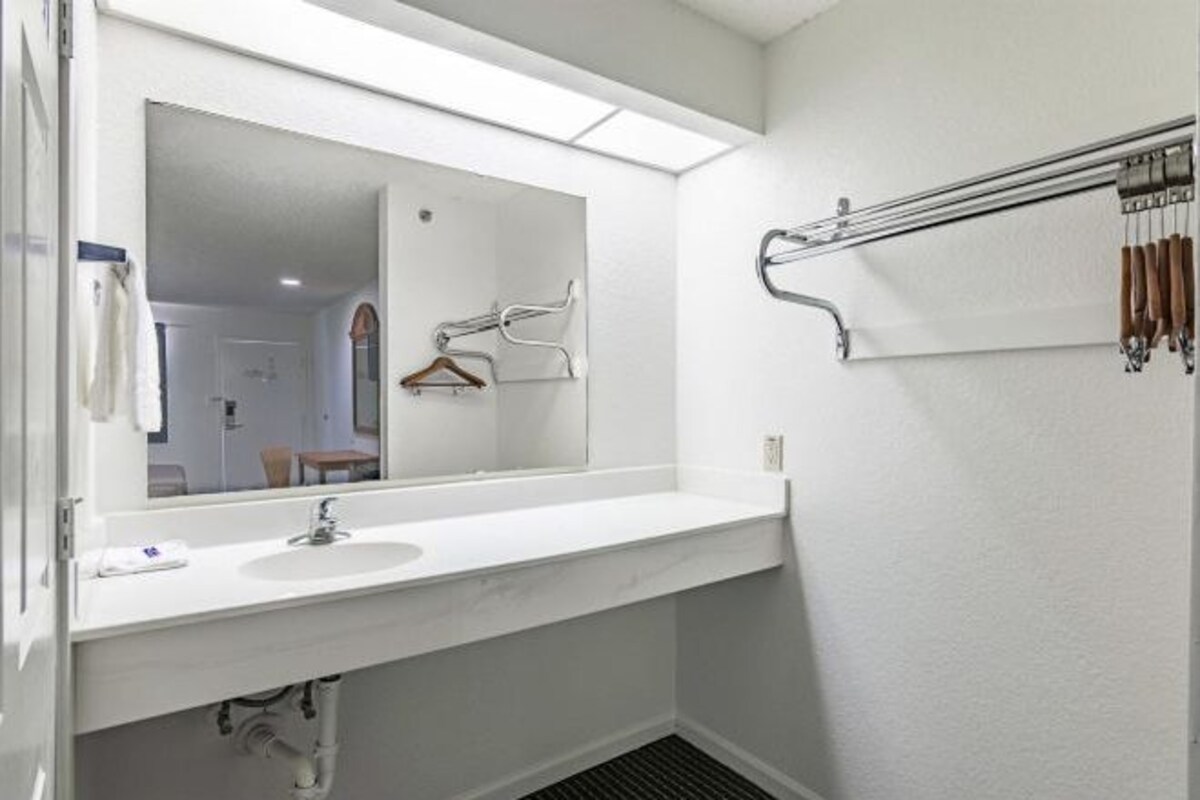 A bathroom with a white sink, a large mirror, and a towel rack with hangers.