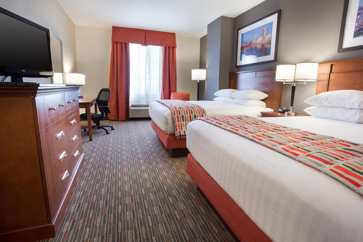 Ein Hotelzimmer mit einem großen Bett, einem Schreibtisch mit Stuhl, einem Fernseher und einem Fenster mit Vorhängen.